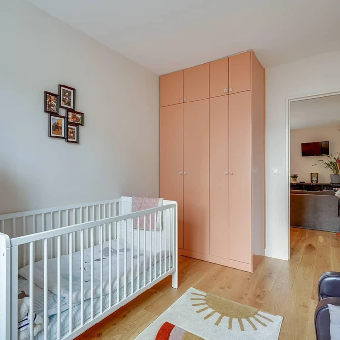 Chambre de bébé moderne avec lit à barreaux blanc, armoire haute couleur pêche à quatre portes et compartiments supérieurs