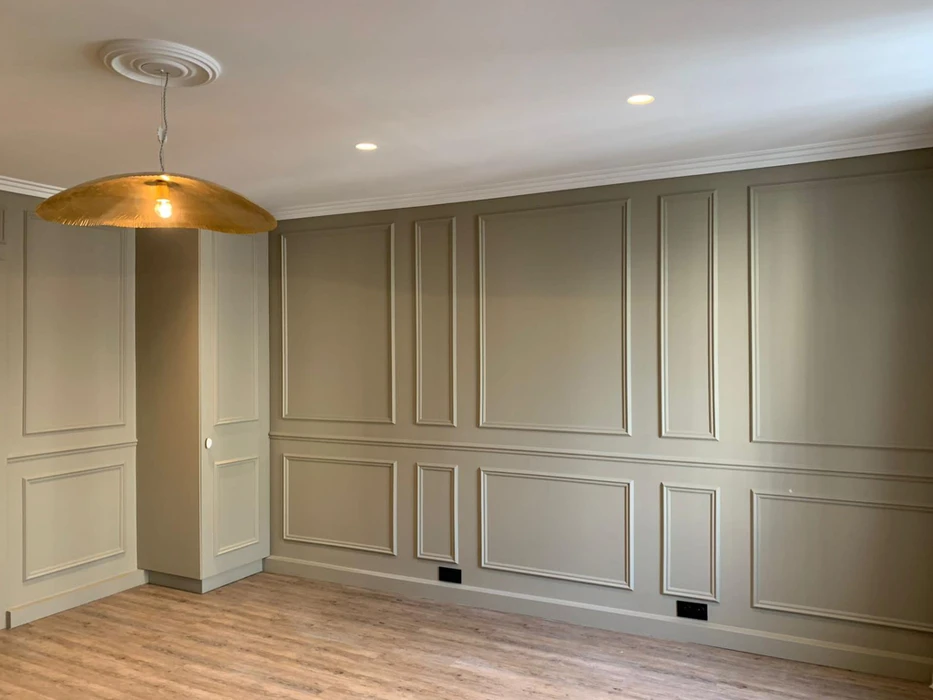 Intérieur résidentiel avec lambris muraux peints en gris-beige, comprenant boiseries décoratives à panneaux rectangulaires superposés sur deux niveaux