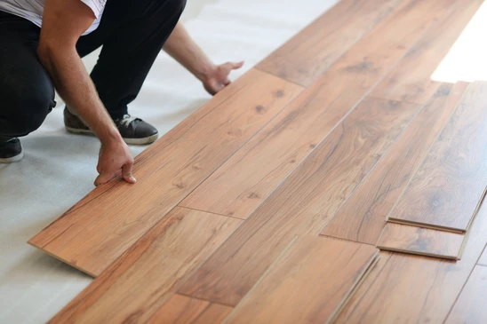 Un homme à genoux installe un parquet flottant en lames de bois dans un intérieur
