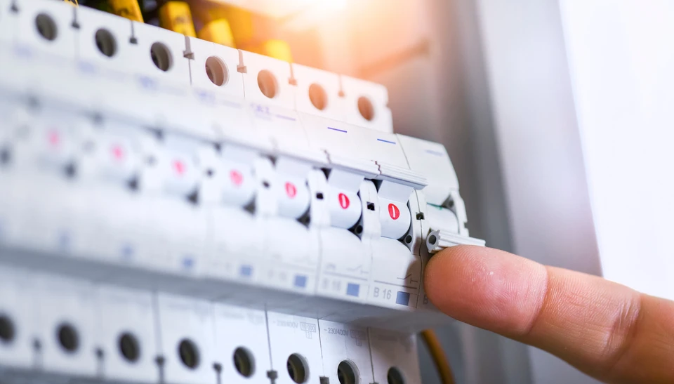 Intérieur professionnel, technicien en veste bleue effectuant mesures électriques sur tableau de distribution